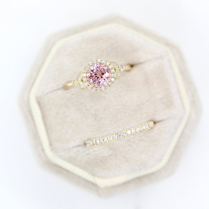 The Cate ring (round) with peachy-pink sapphire in yellow gold with the Elizabeth wedding band in yellow gold in a tan velvet ring box