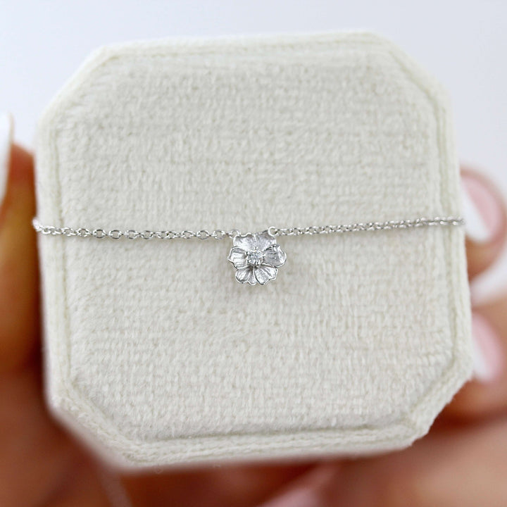a white gold poppy necklace on a white necklace box