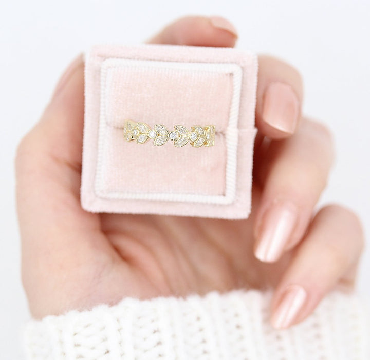 Intricate floral wedding band in 14k yellow gold in a pink velvet ring box held by a hand