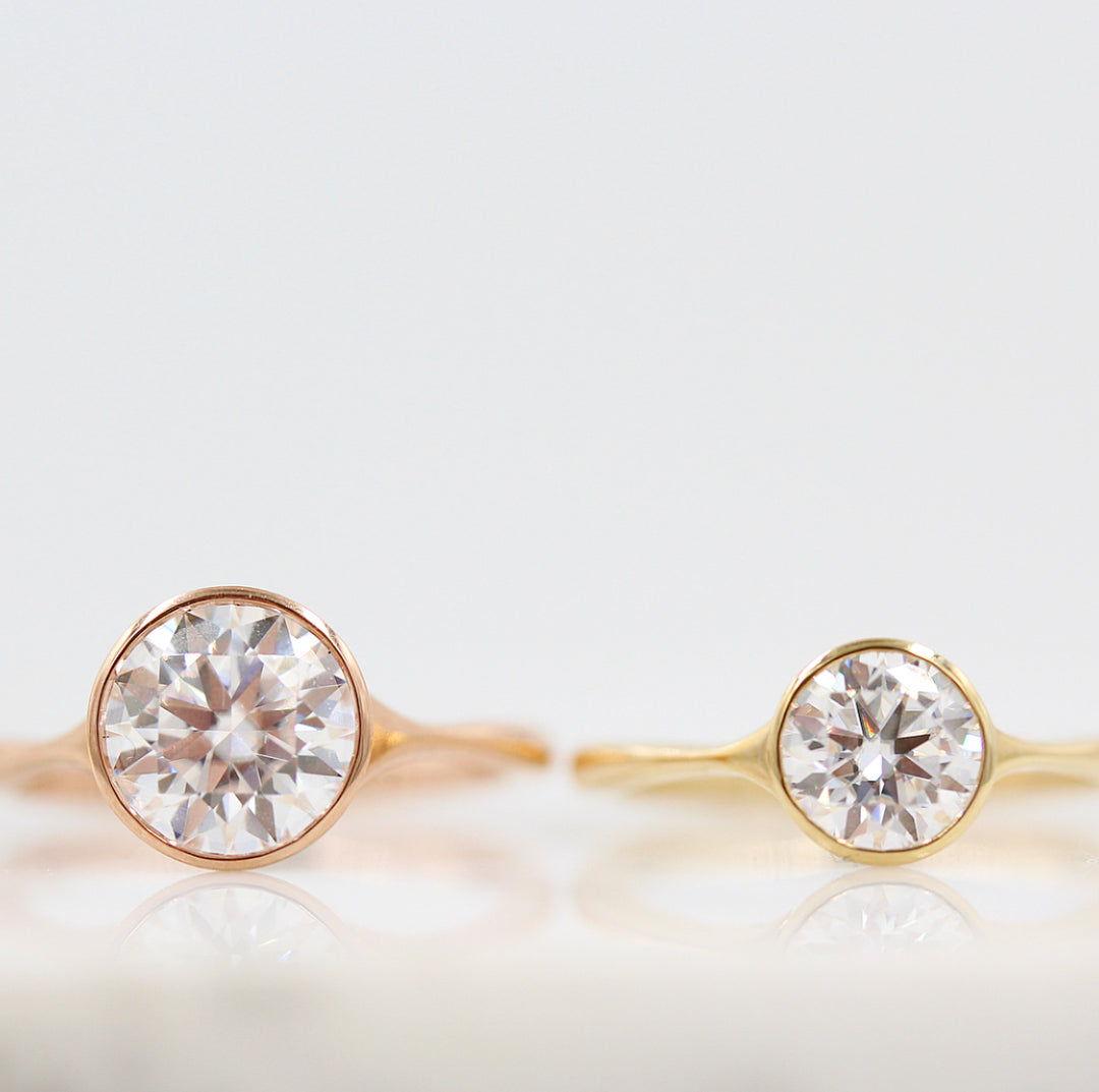 The Stevie Ring (Round) in Rose Gold with 2ct next to the Stevie Ring (Round) in Yellow Gold with 1ct against a white background