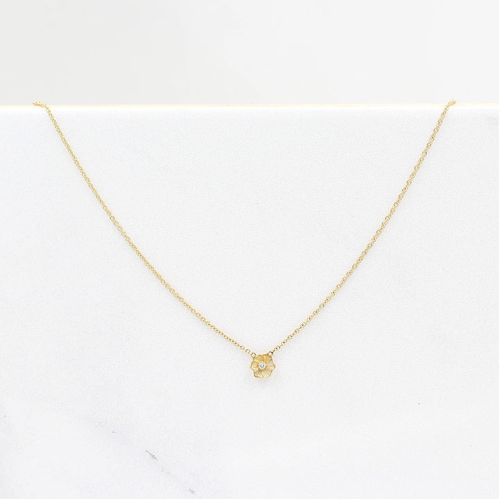 a gold poppy flower necklace on a white surface
