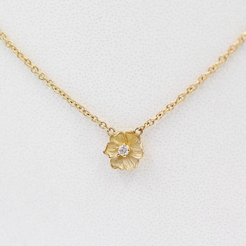 a close-up of a gold poppy flower necklace on a white surface