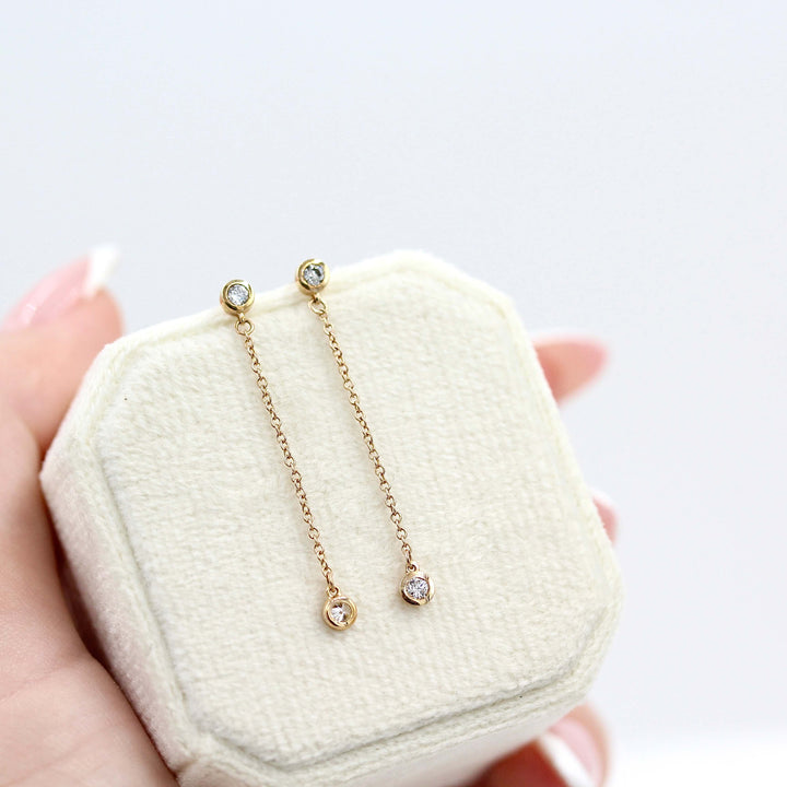 The Diamond Drop Earrings in Yellow Gold on a velvet ring box held by a hand