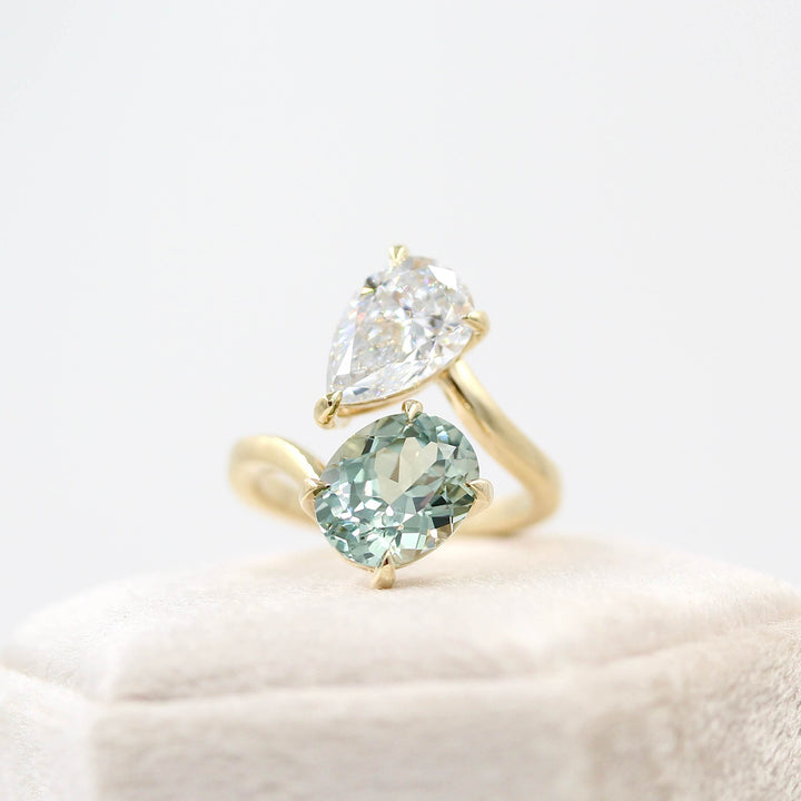 Engagement Ring 14k Yellow Gold Toi Et Moi Diamond and Sage Green Sapphire Bypass Ring in Yellow Gold atop of a tan velvet ring box