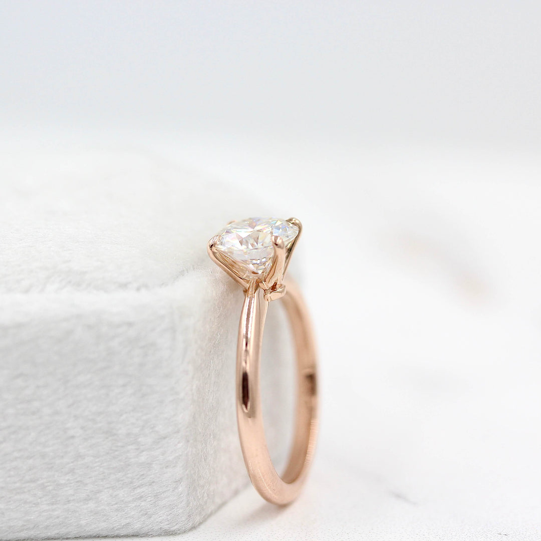 The Margot ring (round) in rose gold leaning against a white velvet ring box