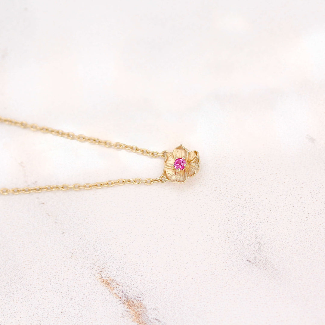 The January Poppy Birthstone Necklace with Padparadscha Sapphire in Yellow Gold atop of a white velvet ring box
