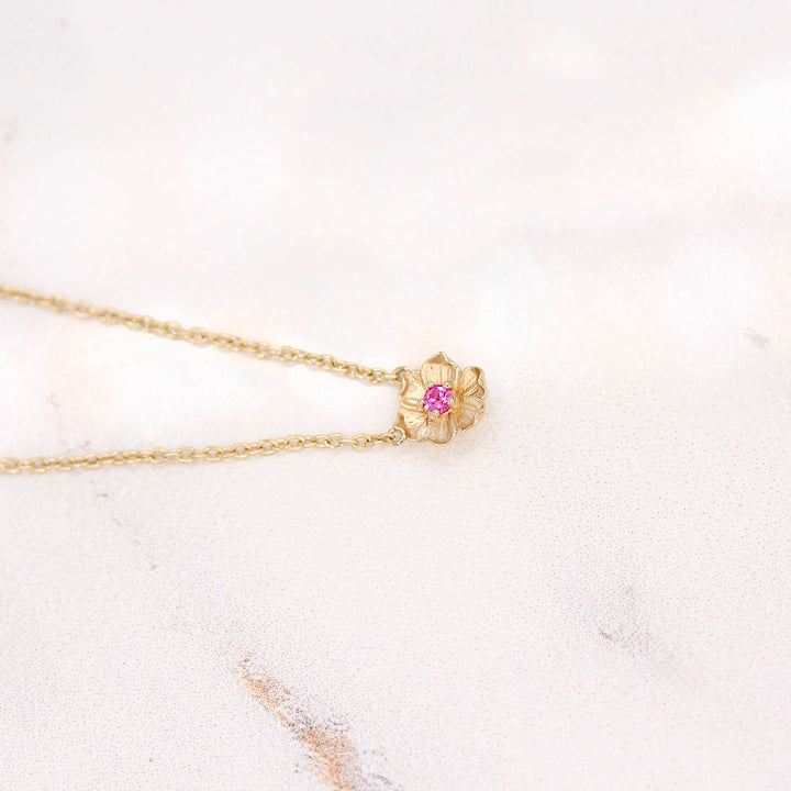 The January Poppy Birthstone Necklace with Padparadscha Sapphire in Yellow Gold atop of a white velvet ring box