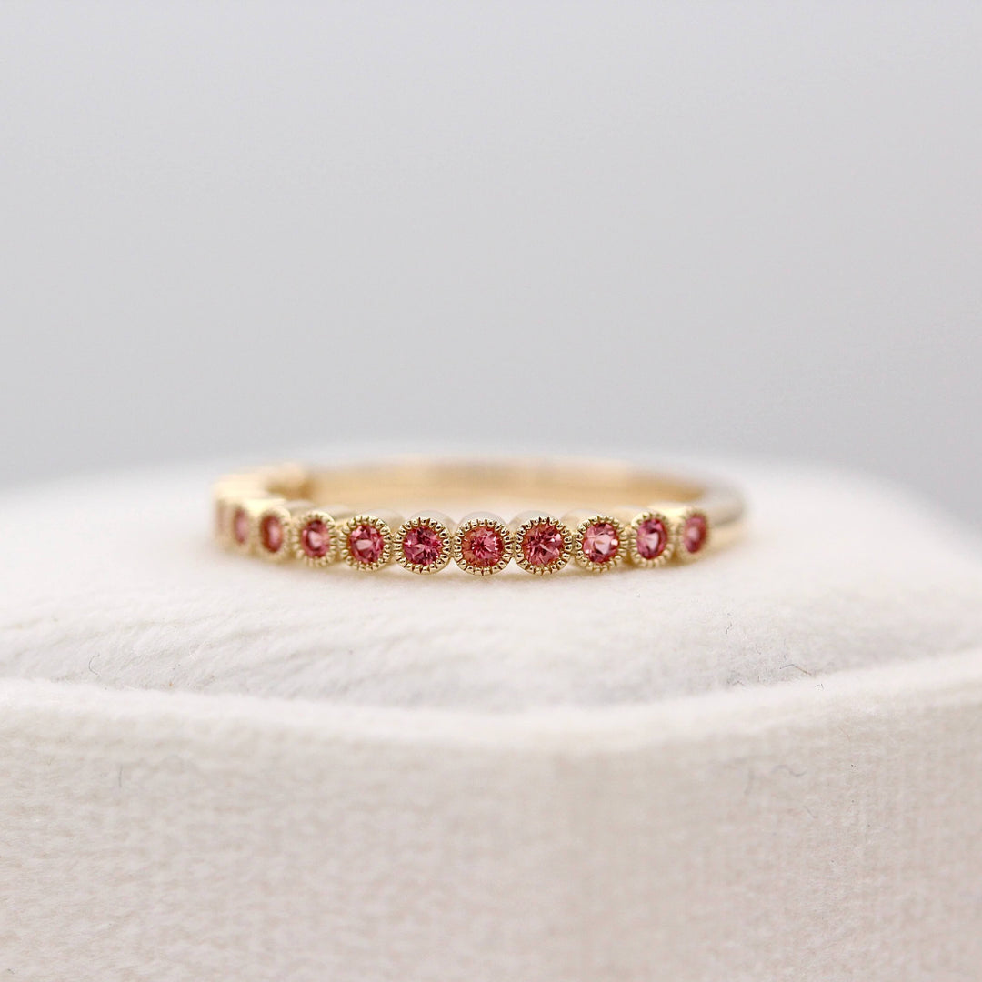 The January Florence Birthstone Wedding Band with Padparadscha Sapphire in Yellow Gold atop of a white velvet ring box