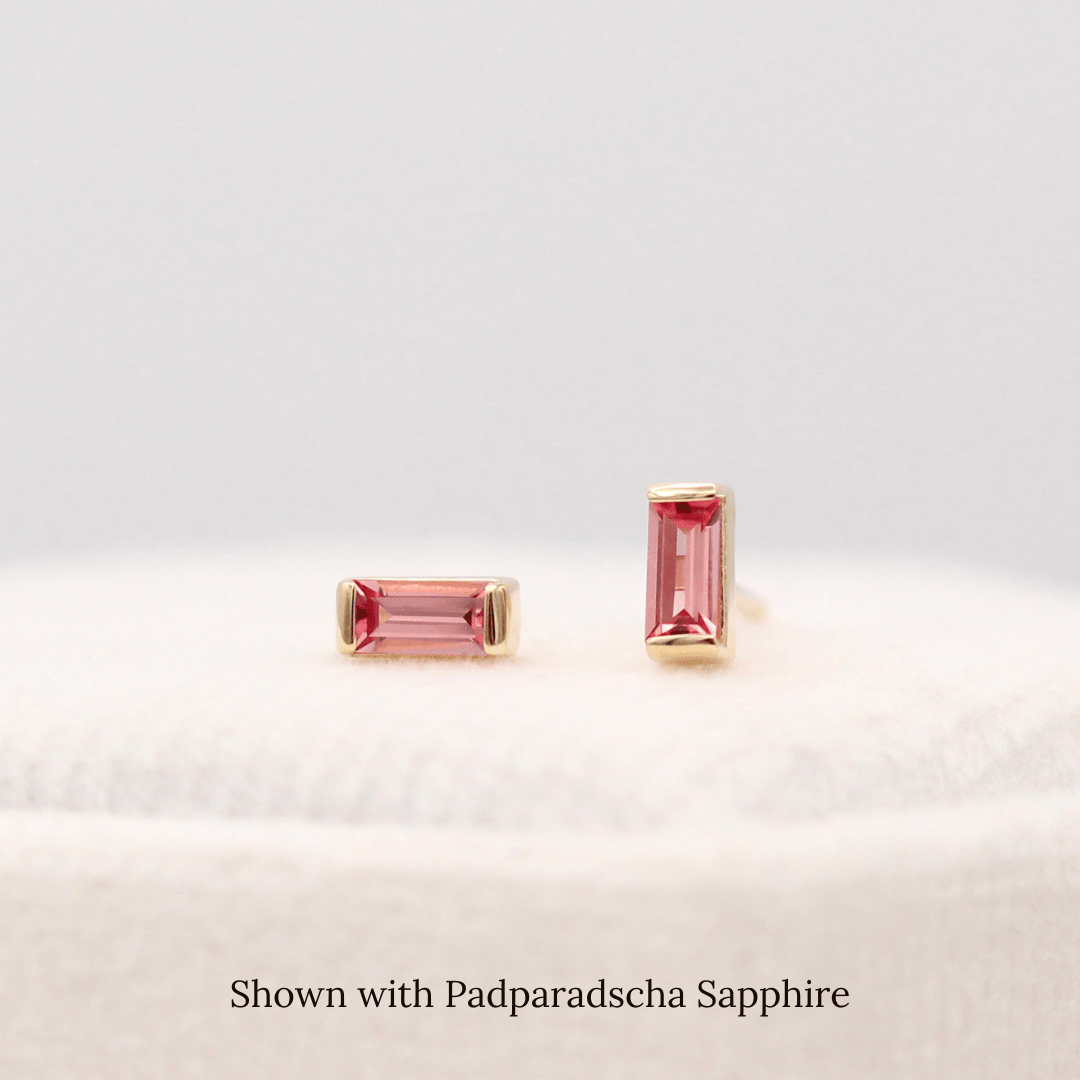 The January Baguette Birthstone Earrings with Padparadscha Sapphire in Yellow Gold atop of a white velvet ring box