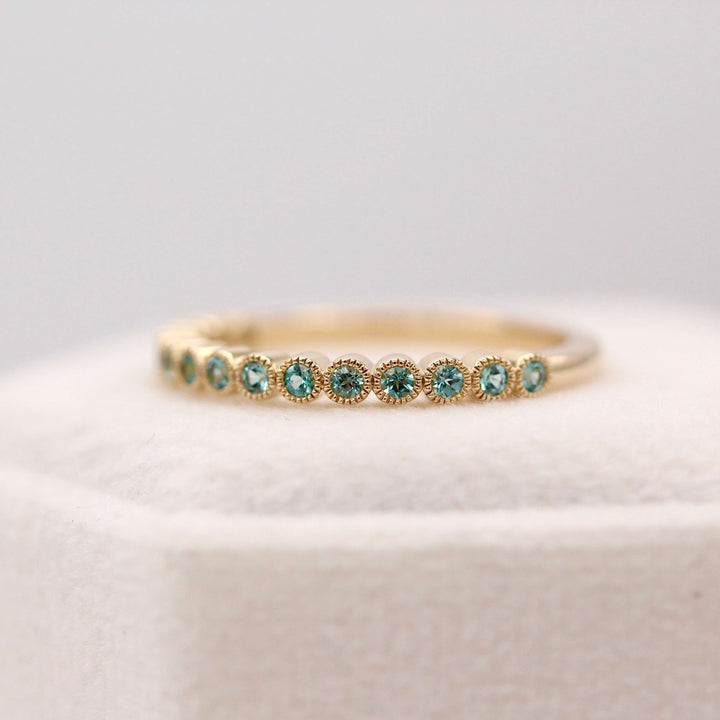 The December Florence Birthstone Wedding Band with Paraiba Spinel in Yellow Gold atop of a white velvet ring box