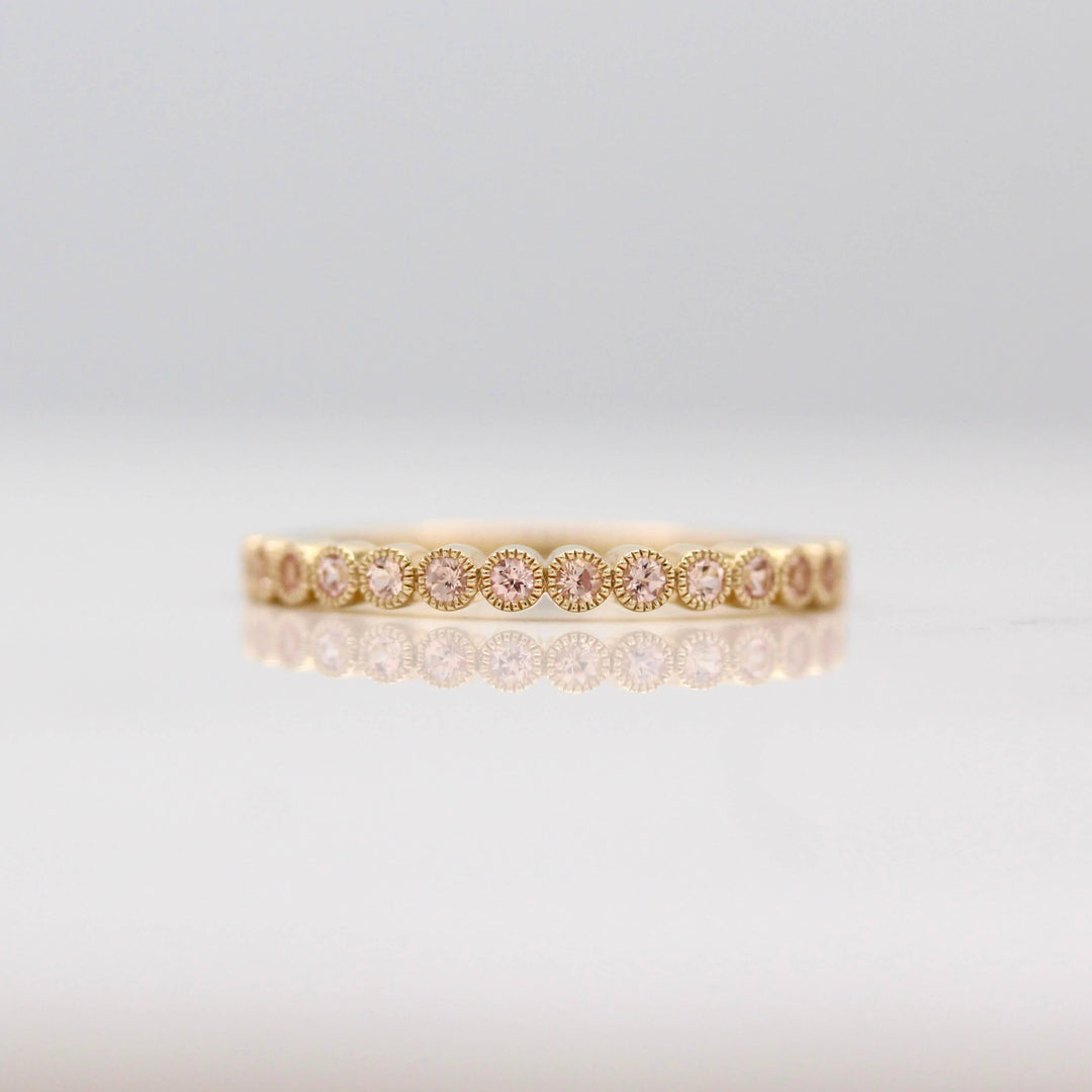 The October Florence Birthstone Wedding Band with Peachy-Pink Sapphire in Yellow Gold against a white background