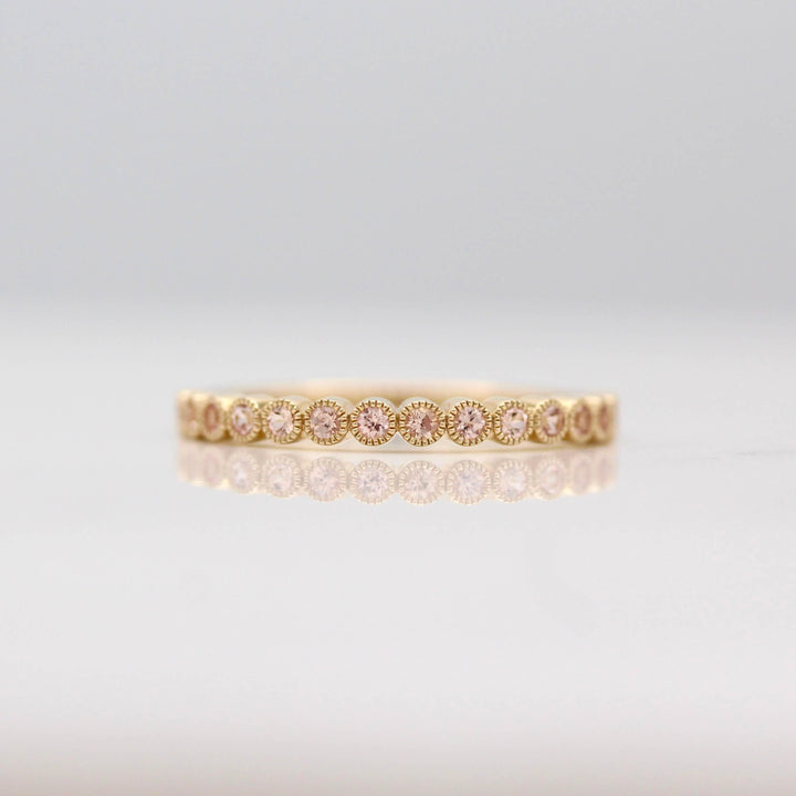 The October Florence Birthstone Wedding Band with Peachy-Pink Sapphire in Yellow Gold against a white background