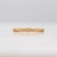 The October Florence Birthstone Wedding Band with Peachy-Pink Sapphire in Yellow Gold against a white background