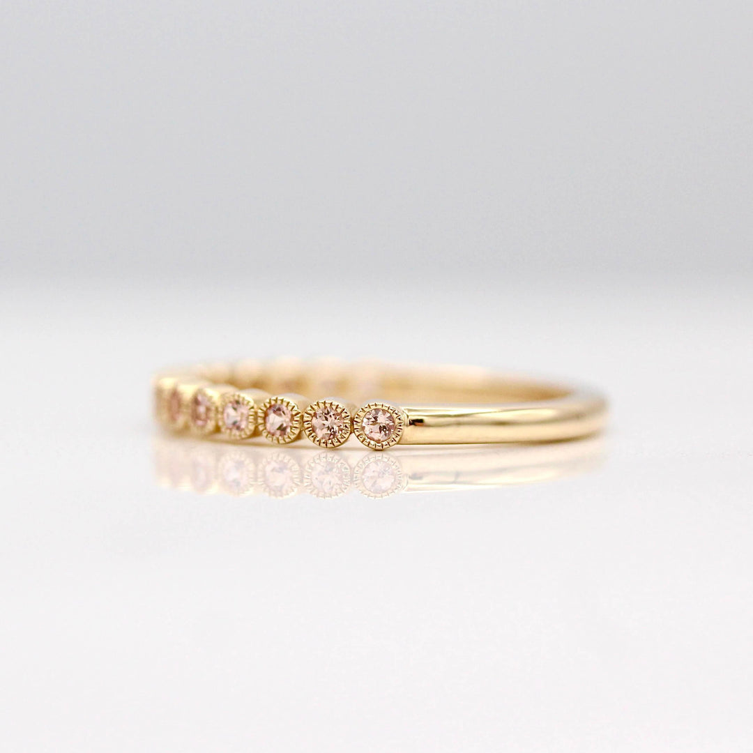 The October Florence Birthstone Wedding Band with Peachy-Pink Sapphire in Yellow Gold against a white background