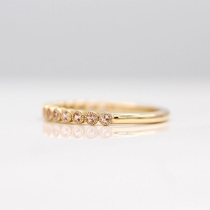 The October Florence Birthstone Wedding Band with Peachy-Pink Sapphire in Yellow Gold against a white background