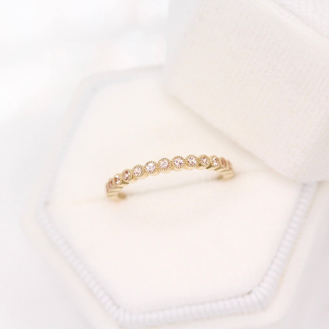 The October Florence Birthstone Wedding Band with Peachy-Pink Sapphire in Yellow Gold in a white velvet ring box