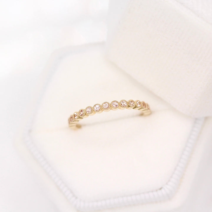 The October Florence Birthstone Wedding Band with Peachy-Pink Sapphire in Yellow Gold in a white velvet ring box
