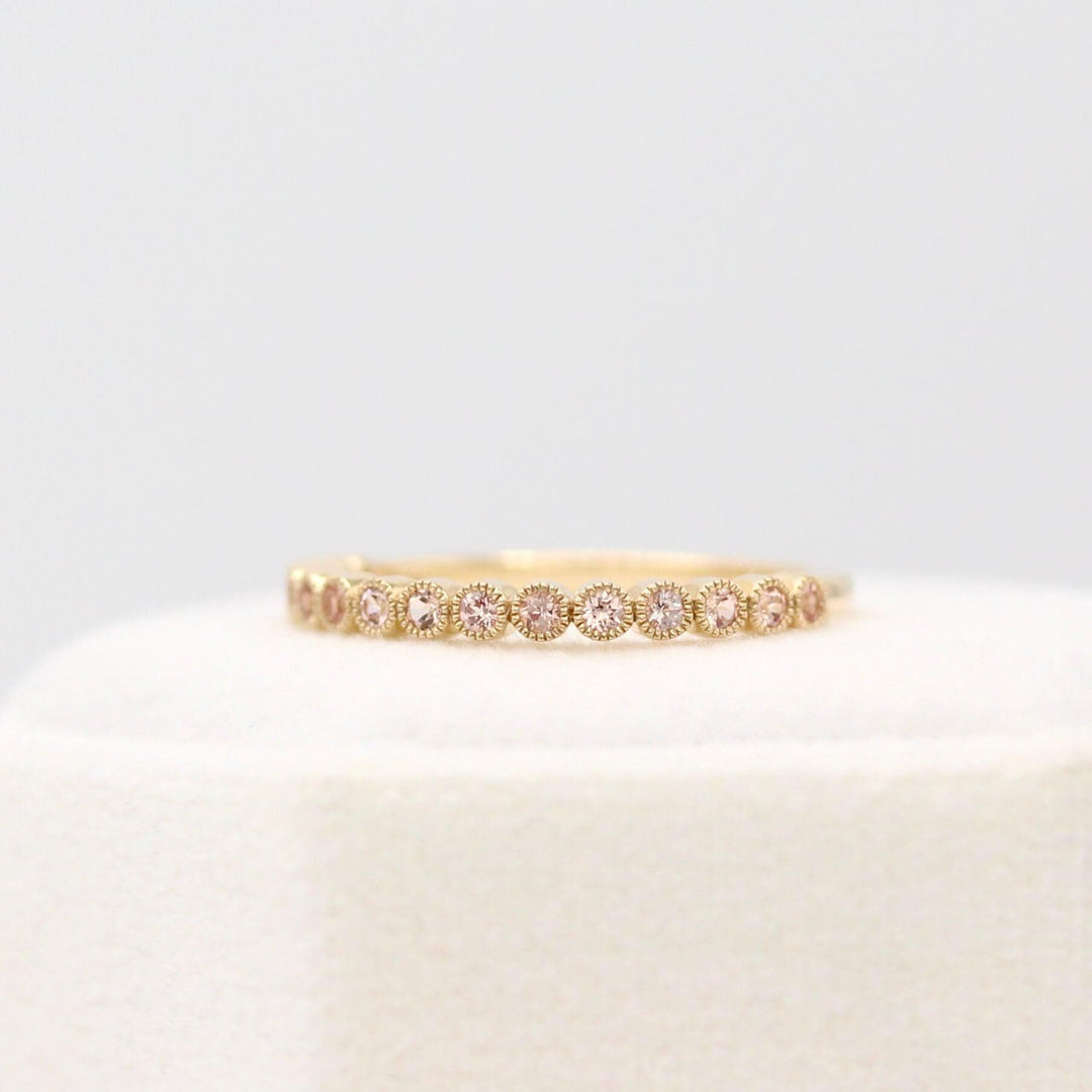 The October Florence Birthstone Wedding Band with Peachy-Pink Sapphire in Yellow Gold in a white velvet ring box