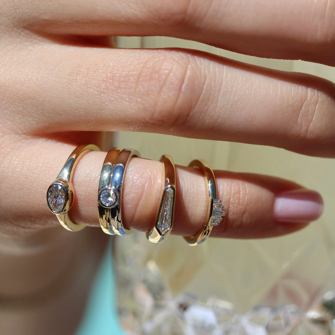 Four fun pinky rings on a hand all with different shaped diamond center stones.