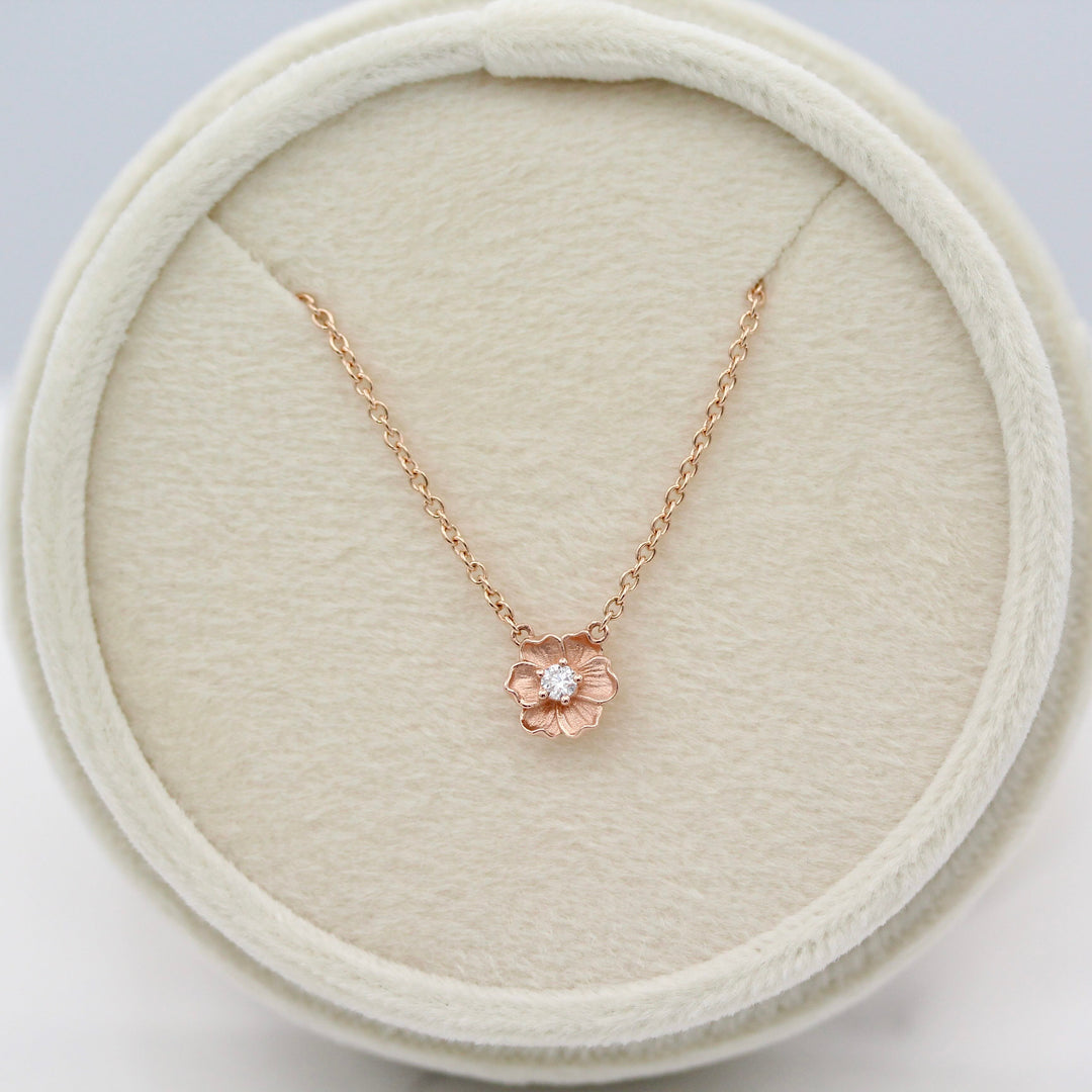 Rose gold necklace with a flower pendant in a round ivory velvet necklace box.