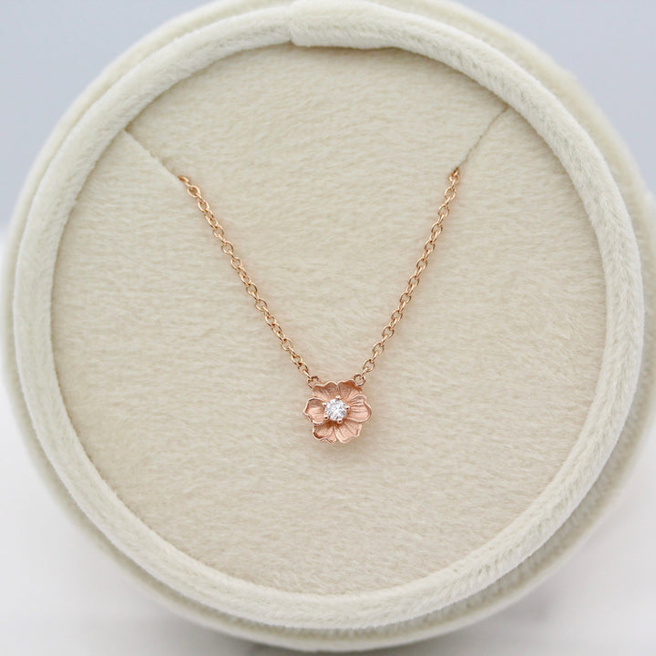 Rose gold necklace with a flower pendant in a round ivory velvet necklace box.
