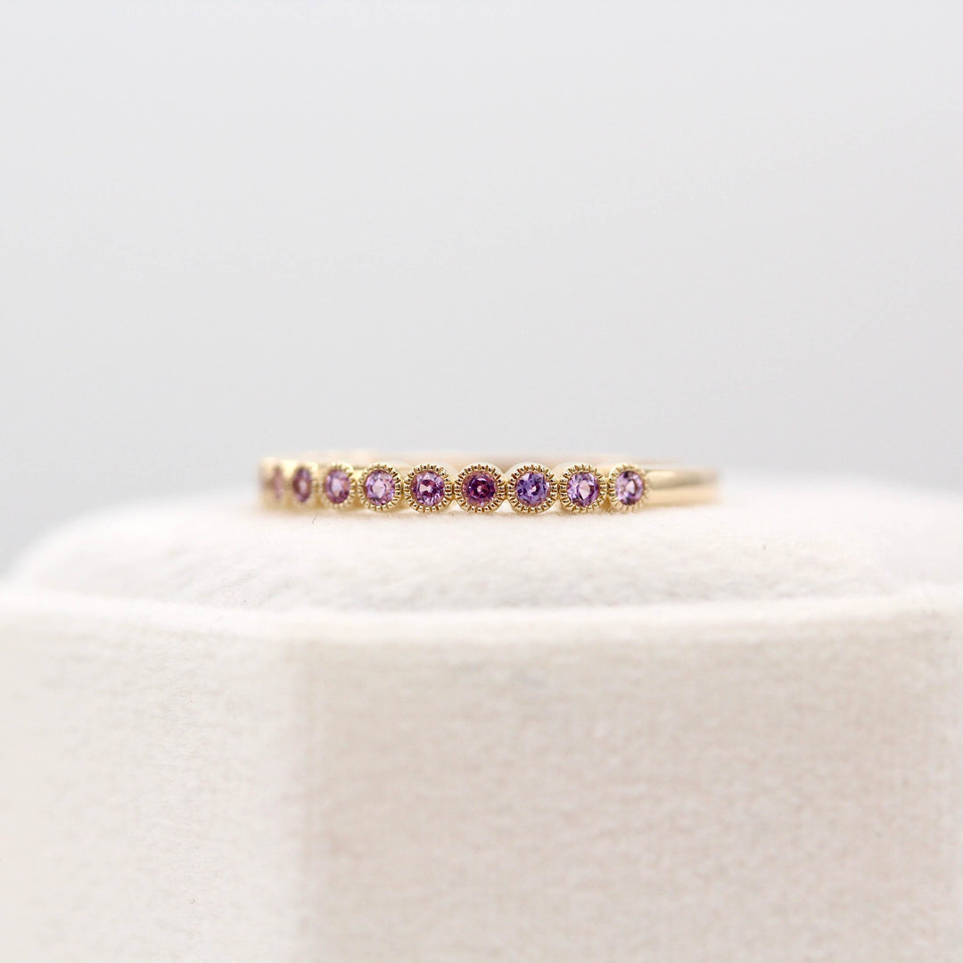 The February Florence Birthstone Wedding Band with Purple Sapphire in Yellow Gold atop of a white velvet ring box