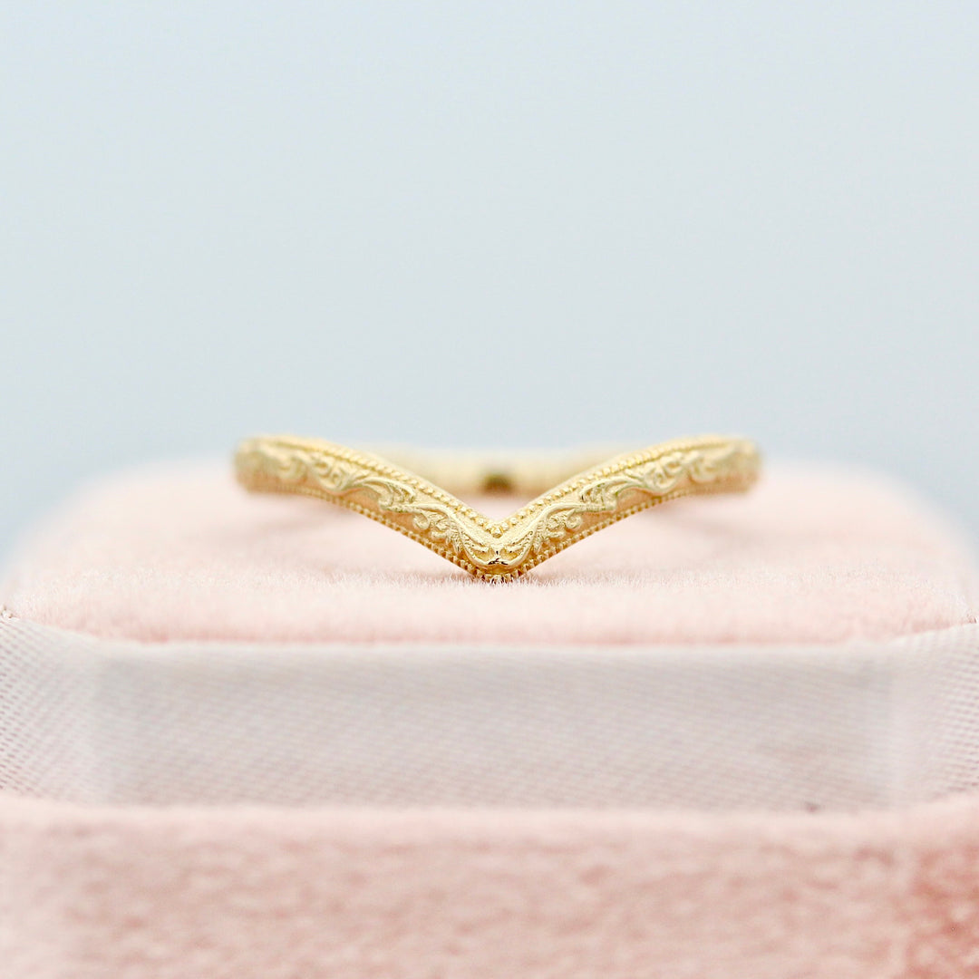 Gold V Shape Wedding Band with Intricate Design resting on a Pink Velvet Ring Box