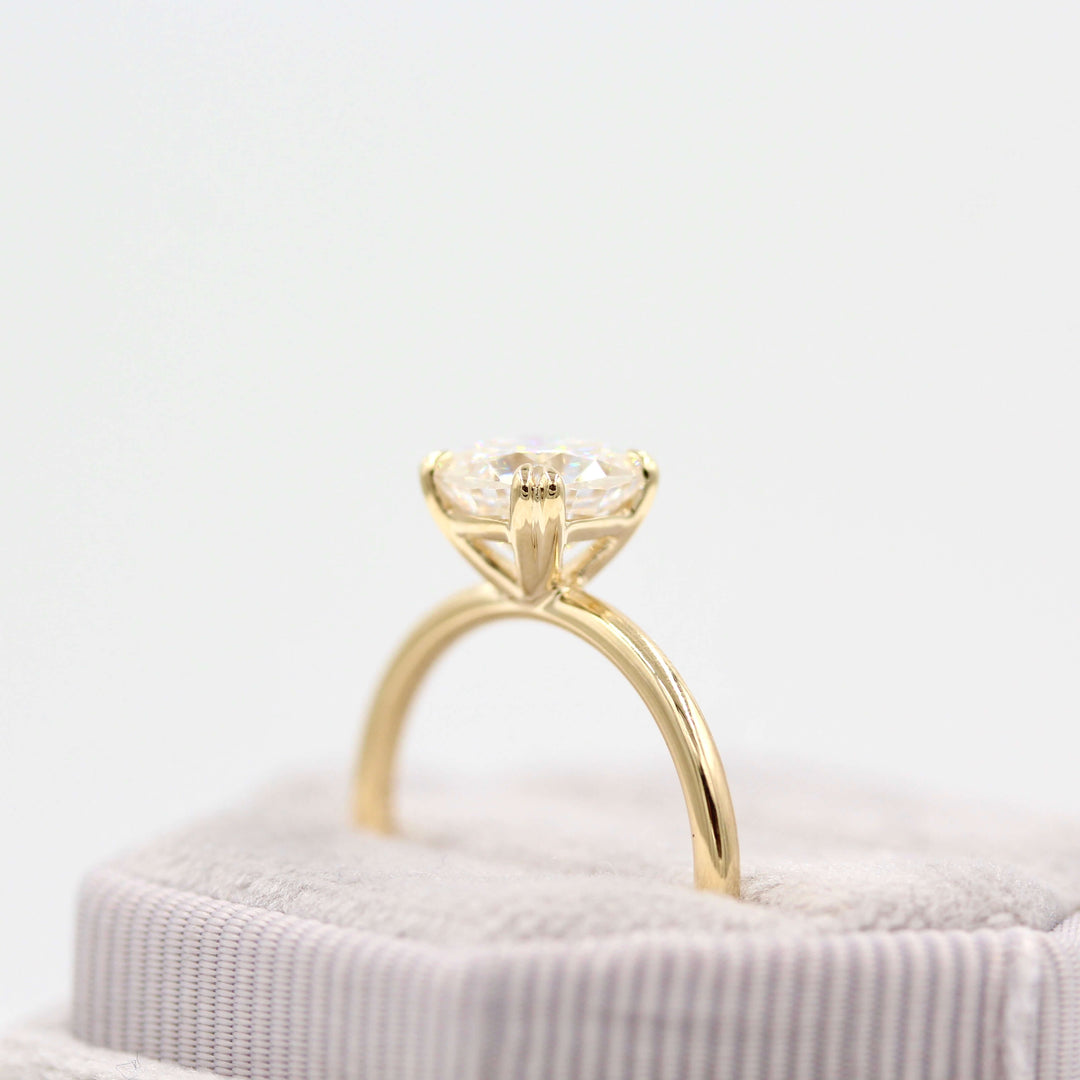 Grey velvet ring box holding 14k yellow gold solitaire cushion engagement ring