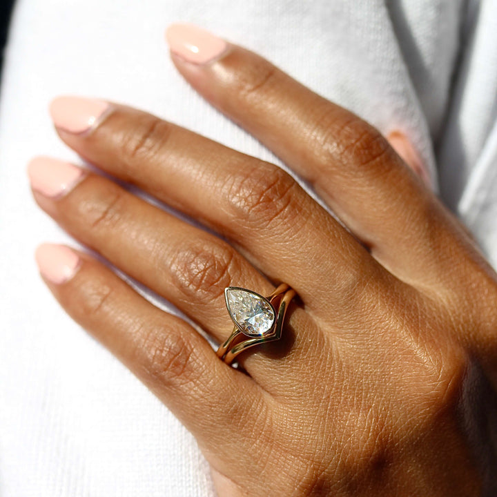 The Stevie Ring (Pear) in Yellow Gold stacked with the V wedding band in yellow gold modeled on a hand