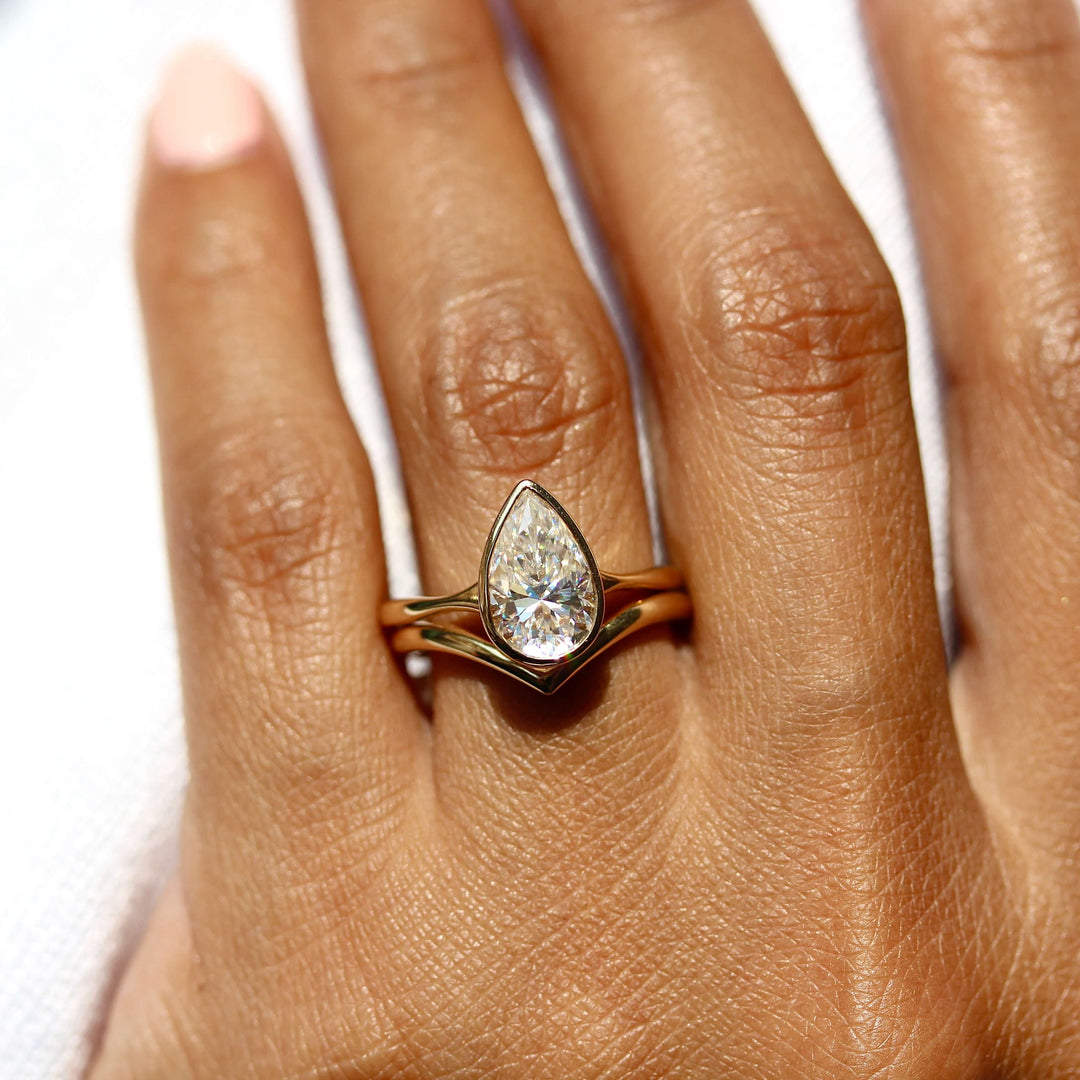 The Stevie Ring (Pear) in Yellow Gold stacked with the V wedding band in yellow gold modeled on a hand