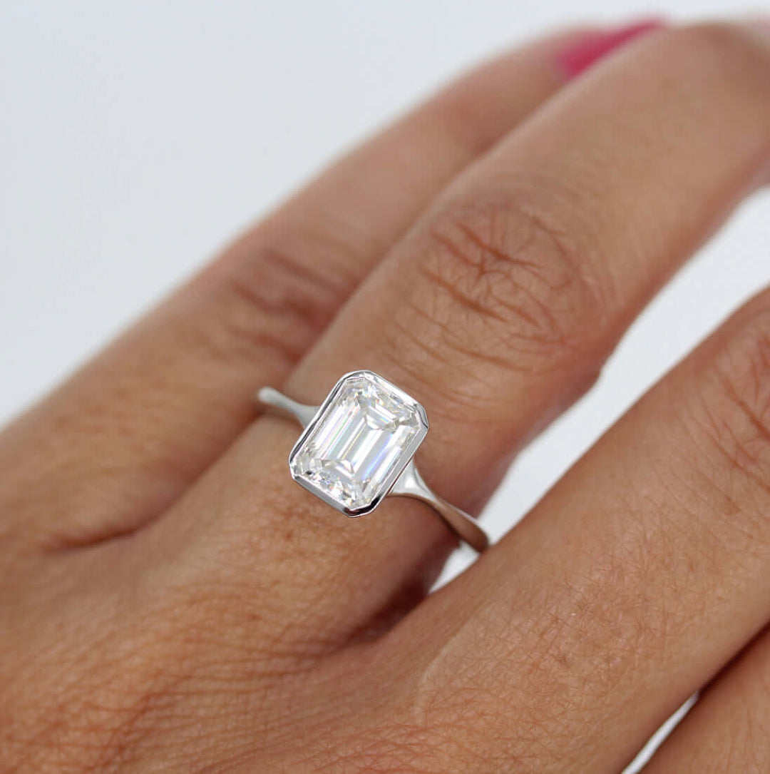 Hand wearing emerald-cut moissanite in a delicate white gold bezel ring