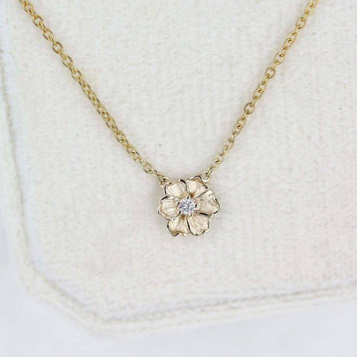 a close-up of a gold poppy necklace in a jewelry box