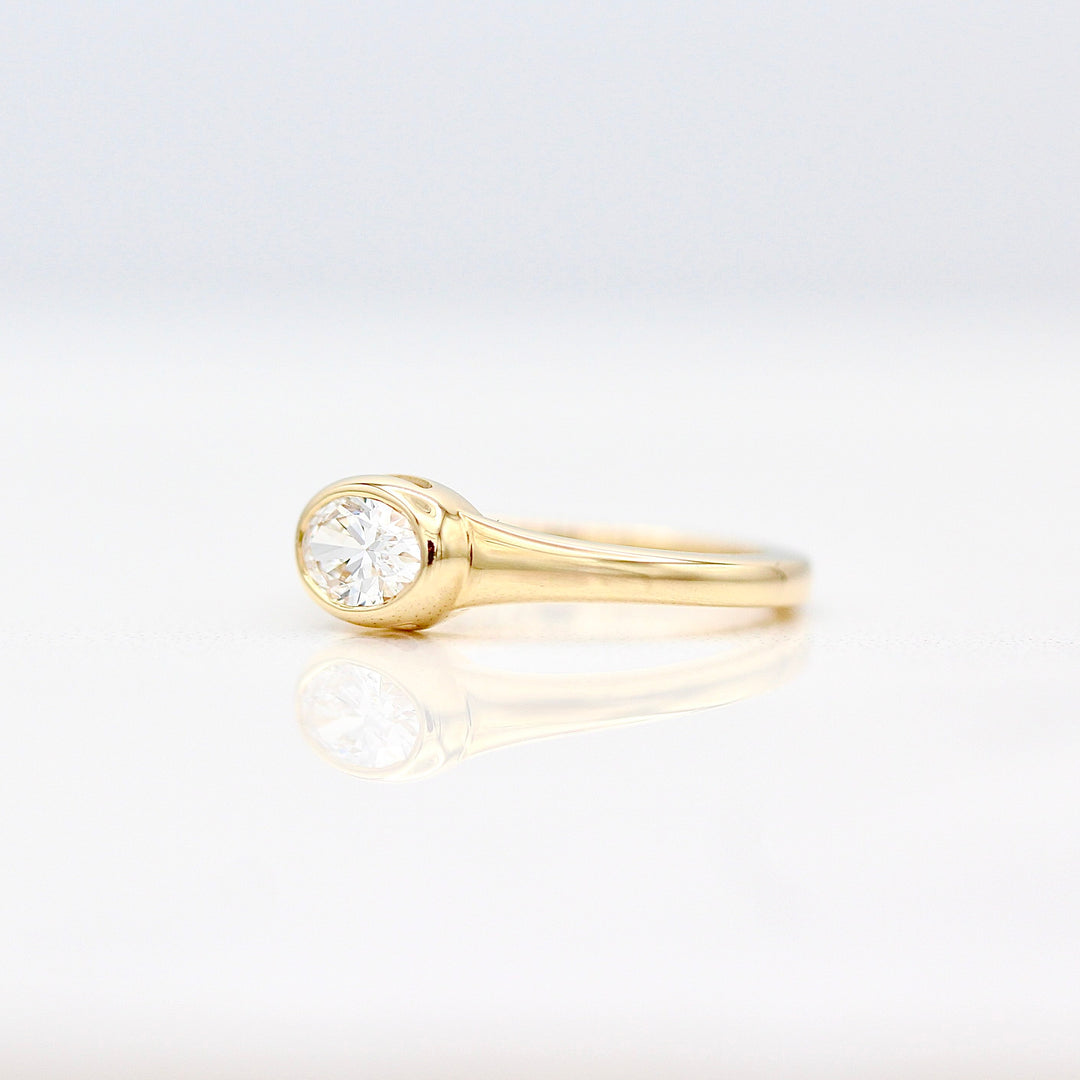 An angled view of an east-west oval diamond pinky ring on a white background