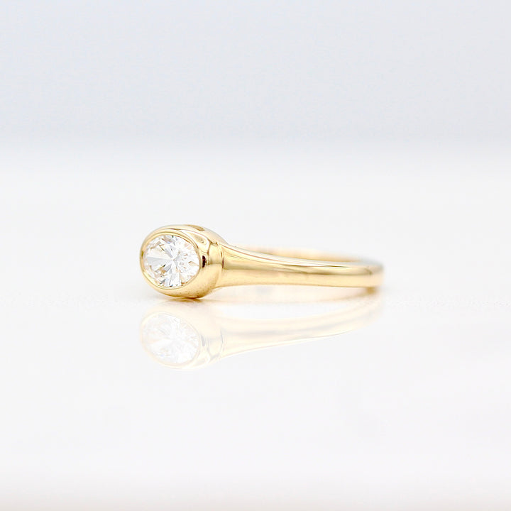 An angled view of an east-west oval diamond pinky ring on a white background