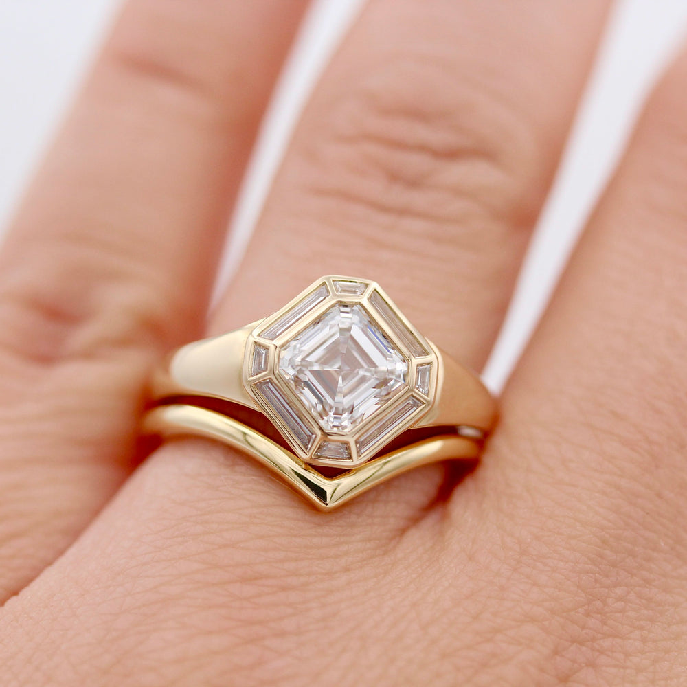 Asscher cut diamond engagement ring with accent stones surrounding the the center diamond in yellow gold stacked with a v shaped wedding band shown on a hand