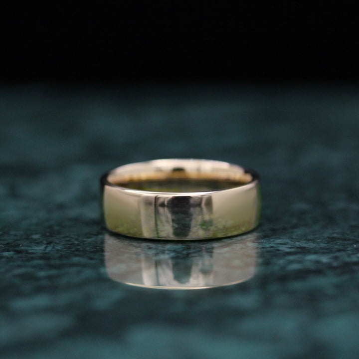 Sleek and reflective yellow gold band on a deep green marble surface with black background