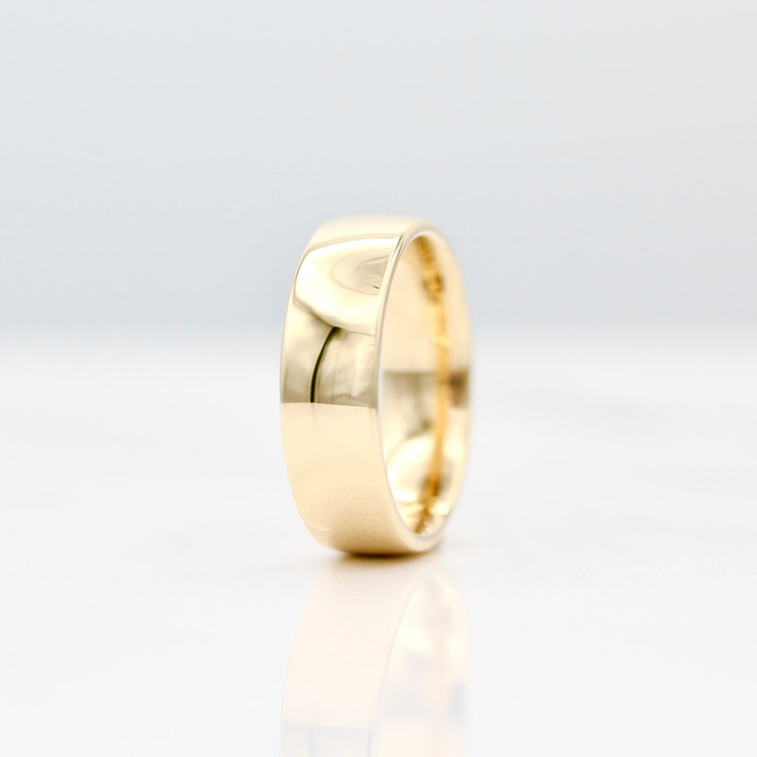 6.5mm Yellow gold sleek band standing on it's side with a white background