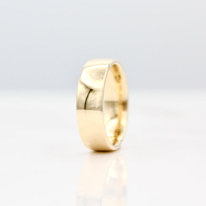 6.5mm Yellow gold sleek band standing on it's side with a white background