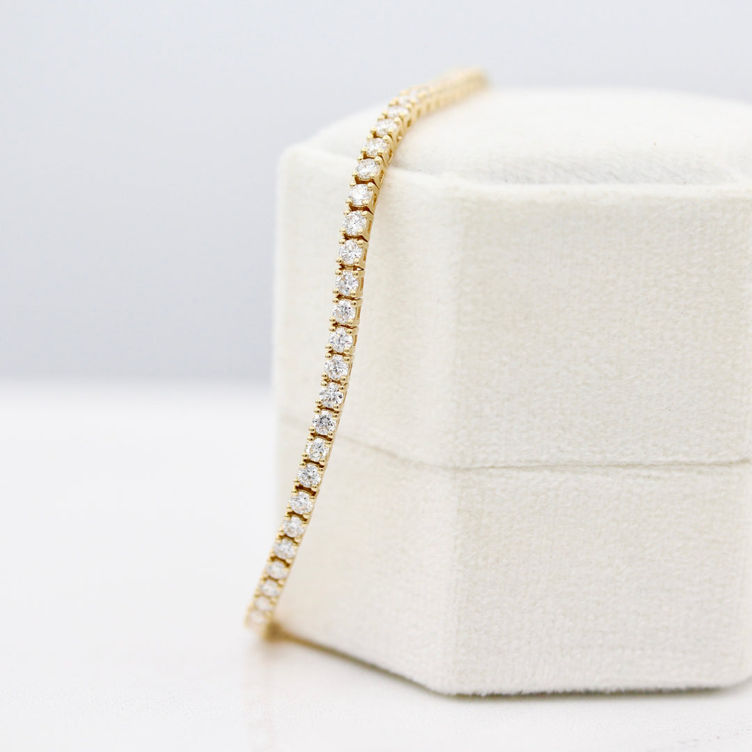 The Classic Lab-Grown Diamond Tennis Bracelet in yellow gold draped over a white velvet ring box