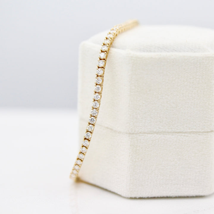 The Classic Lab-Grown Diamond Tennis Bracelet in yellow gold draped over a white velvet ring box