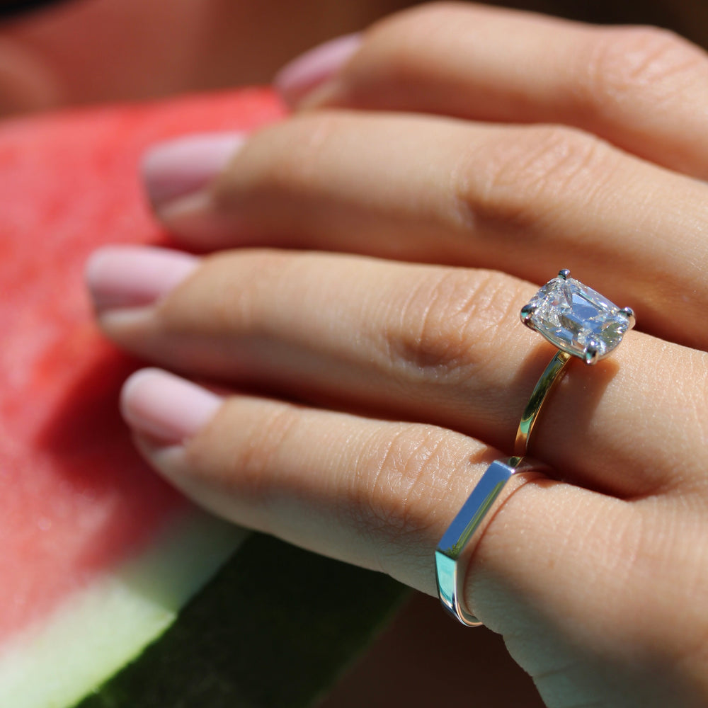 Sterling silver bar signet ring on a hand pictured with a old mind elongated cushion engagement ring, holding a watermelon in the background 