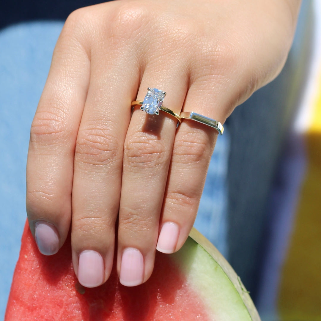 The Eri engagement ring and Eleanor sterling silver bar signet pinky ring on a hand holding a watermelon slice