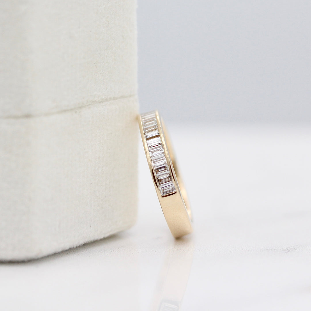 Yellow gold channel set diamond baguette wedding band resting on a white velvet ring box.