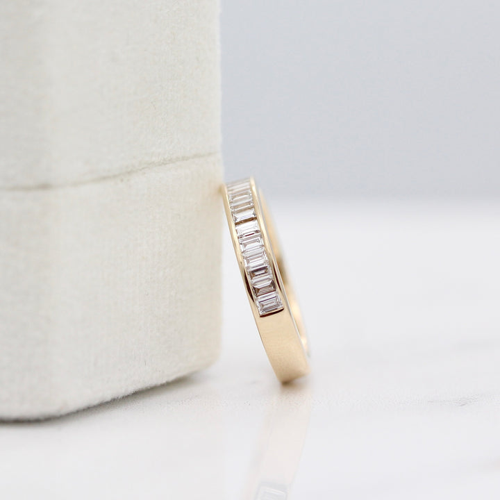 Yellow gold channel set diamond baguette wedding band resting on a white velvet ring box.