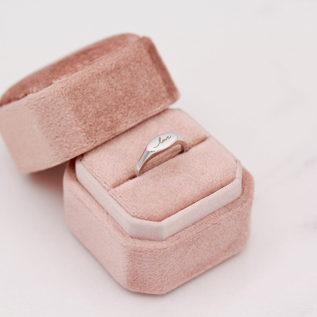 Silver ring with 'love' engraving in a pink jewelry box on a light background