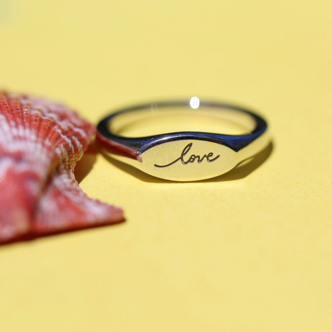 Sterling silver pinky ring with 'love' engraving on a yellow background with an orange sea shell