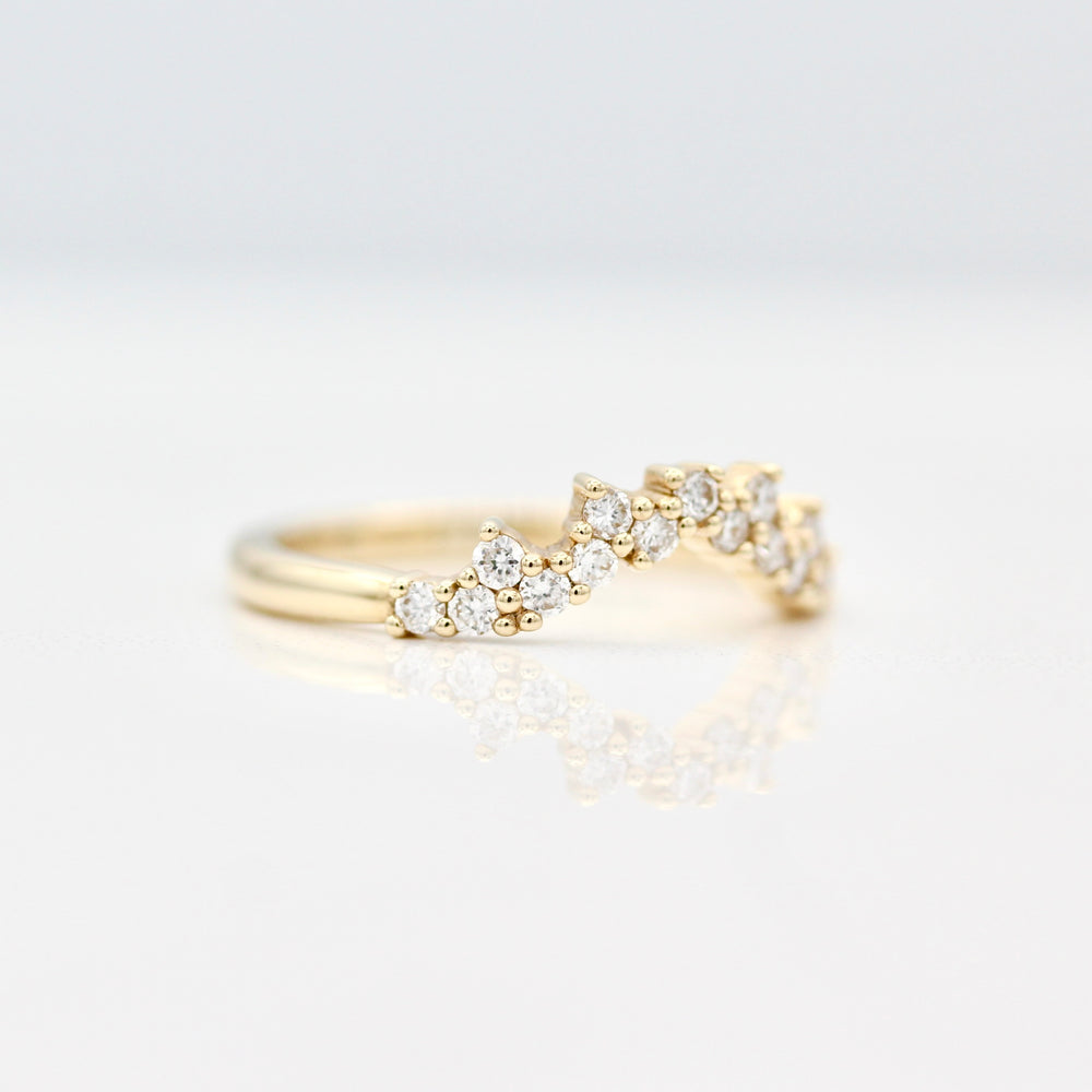 A side view of a yellow gold curved wedding band with prong set round diamond melee