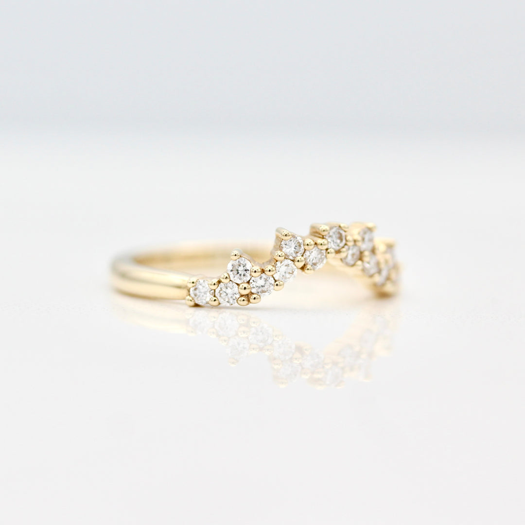 A side view of a yellow gold curved wedding band with prong set round diamond melee