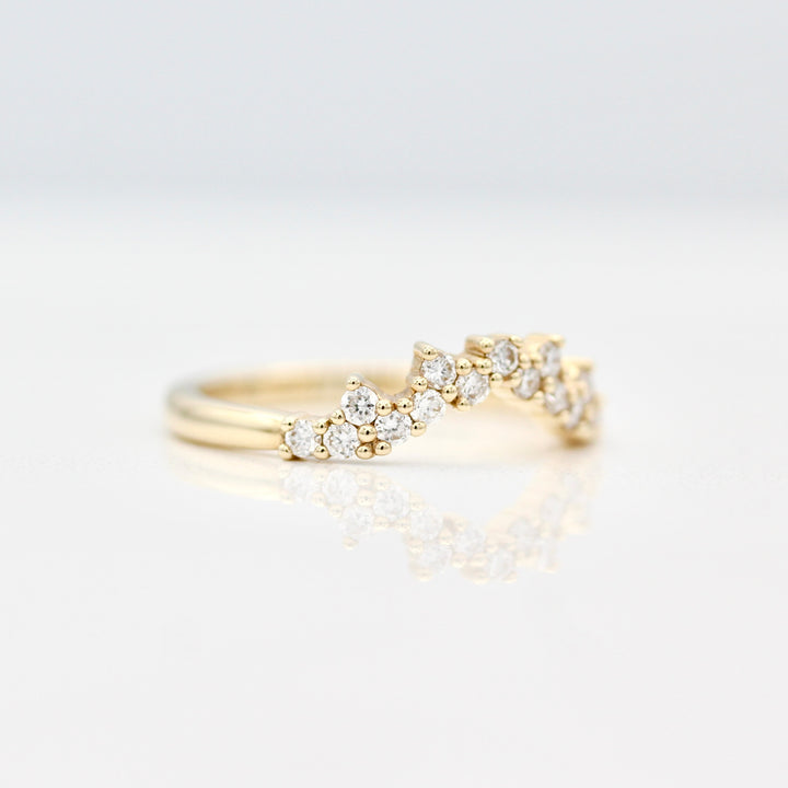 A side view of a yellow gold curved wedding band with prong set round diamond melee