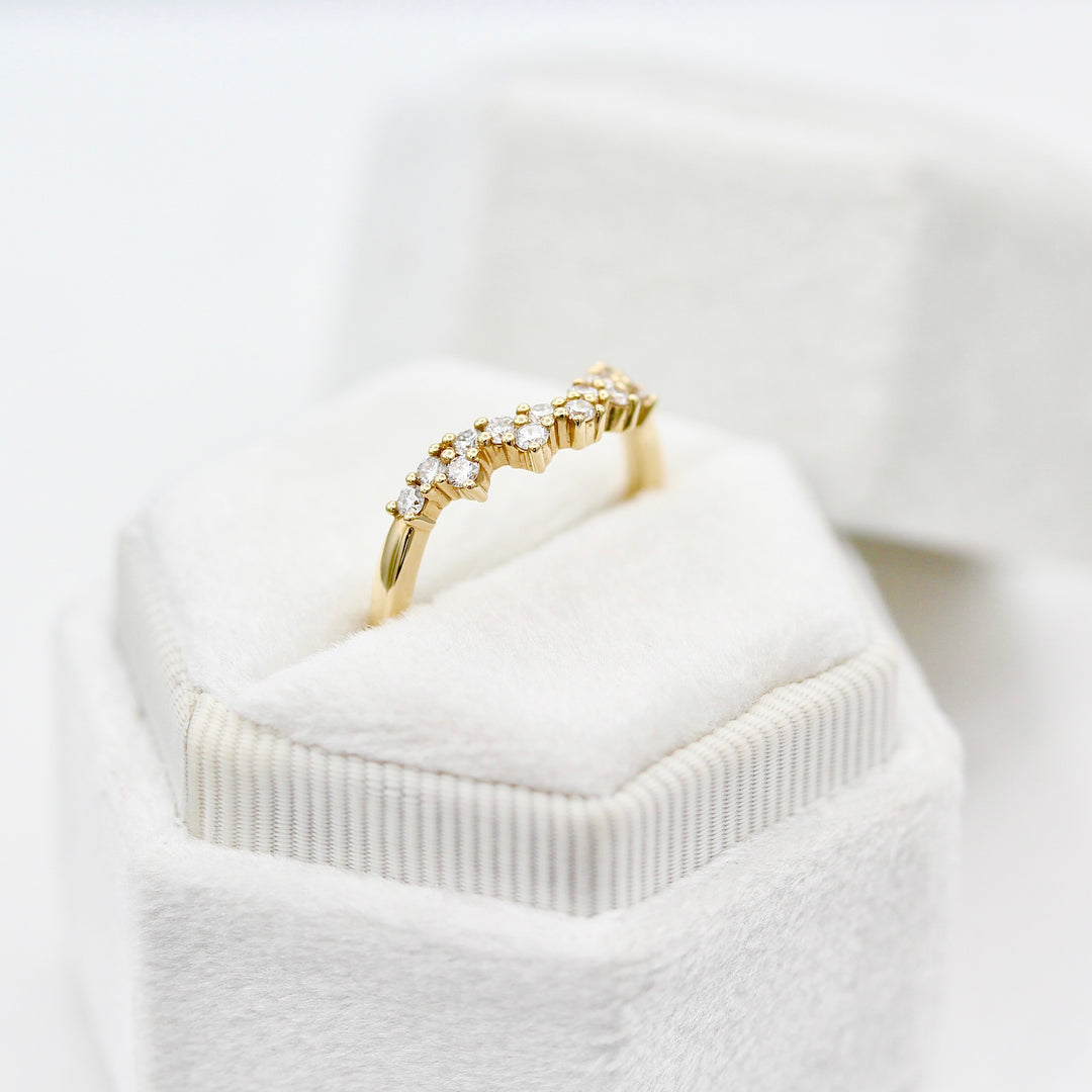 Yellow gold curved wedding band with round diamond melee in a white velvet ring box
